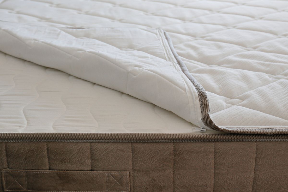 Protector de colchón acolchado blanco ligeramente abierto sobre un colchón con revestimiento marrón