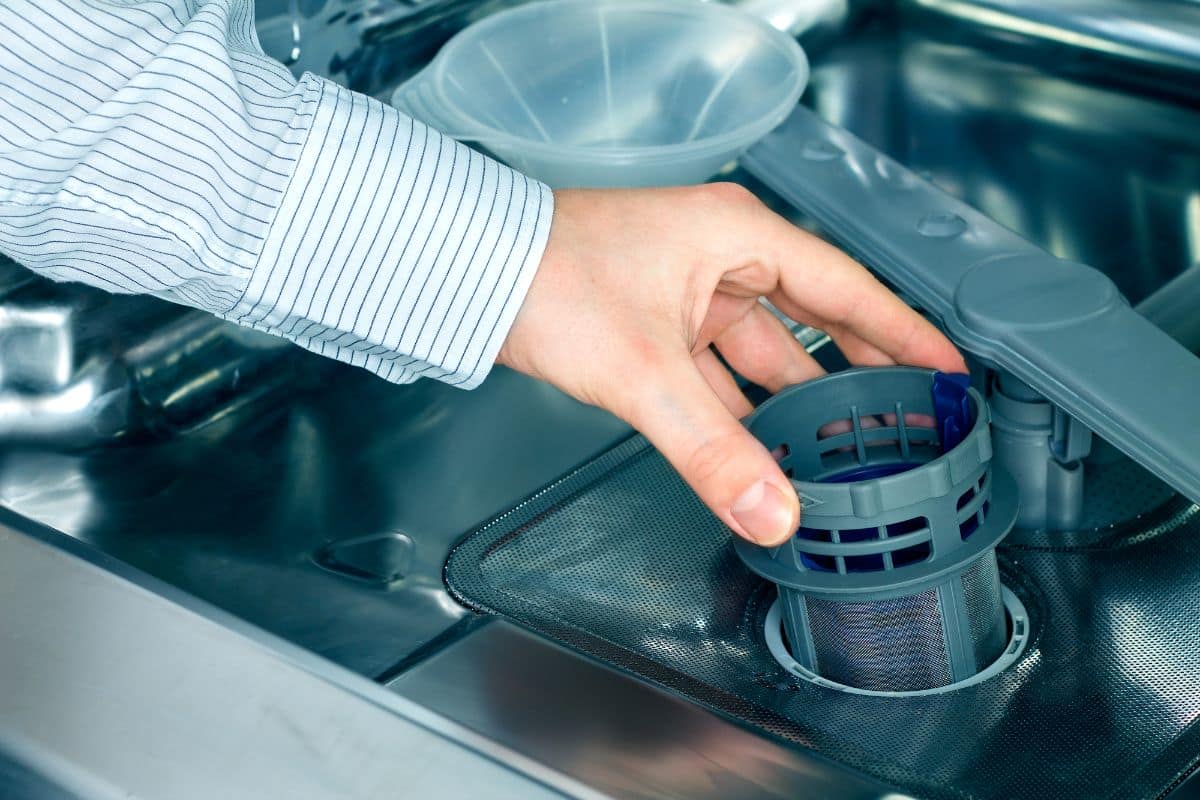 Mano de hombre con camisa a rayas sacando el lavavajillas del lavavajillas
