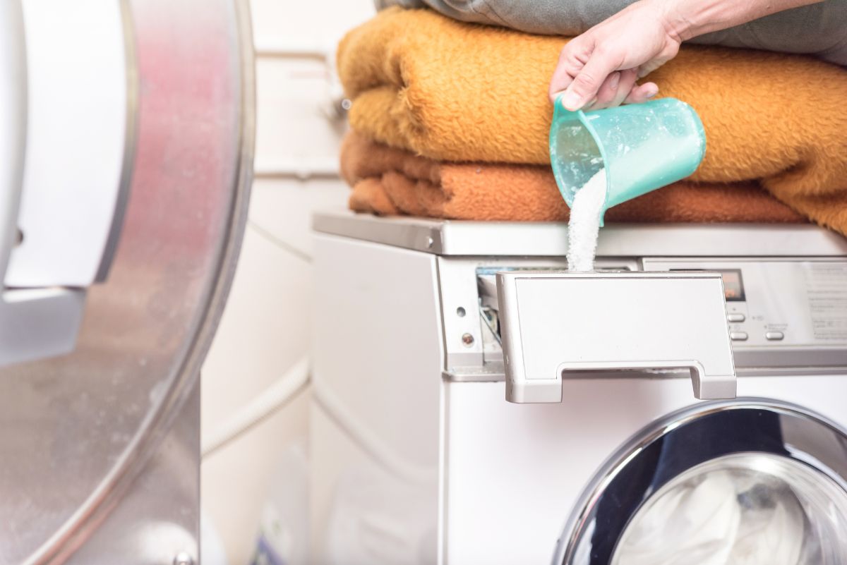 Vertiendo a mano el detergente en la lavadora con las mantas dobladas encima