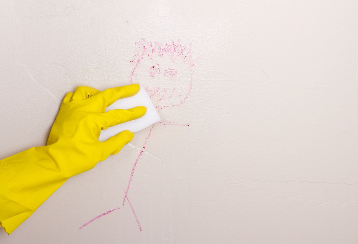 Mano enguantada limpiando crayón de la pared usando un borrador mágico.