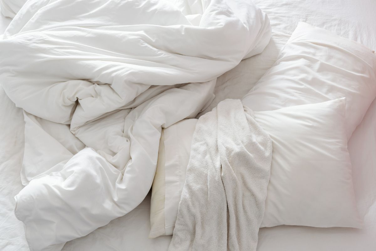 Cama blanca sin hacer con almohadas y sábanas blancas