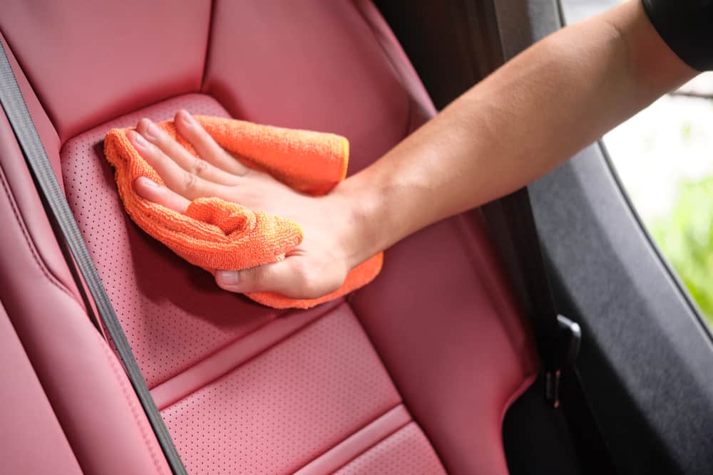 Un hombre limpiando el asiento del coche con un paño de microfibra.