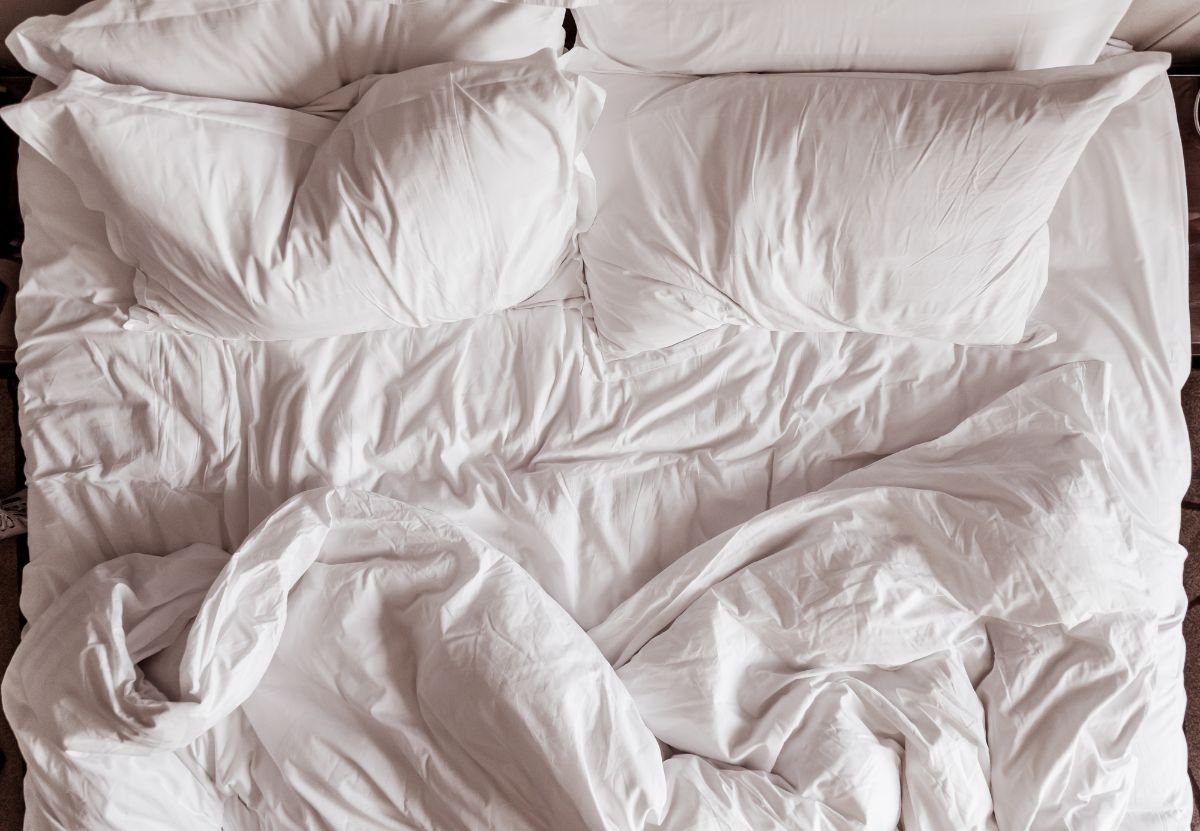 Cama sin hacer con sábanas blancas almohadas y edredón