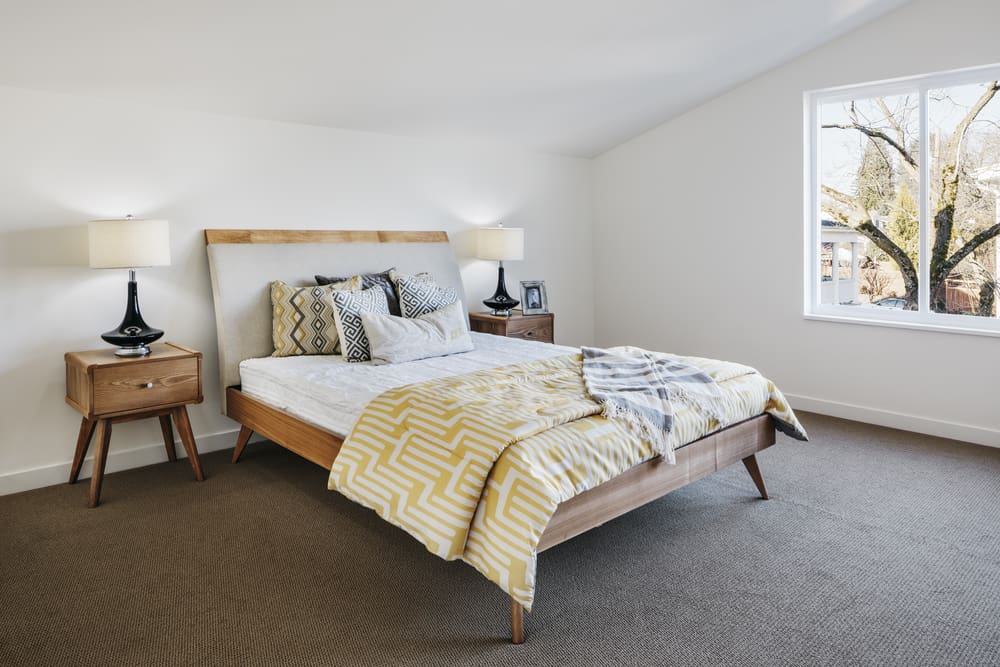 Esta es una vista de cerca de un dormitorio que tiene una cama de plataforma de madera sobre un suelo de moqueta gris.
