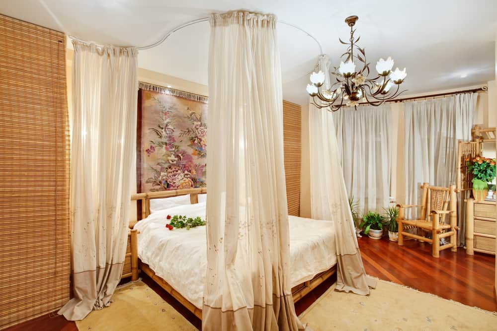 Esta es una vista cercana del dormitorio que tiene una cama hecha de bambú rodeada por un dosel de cortinas.