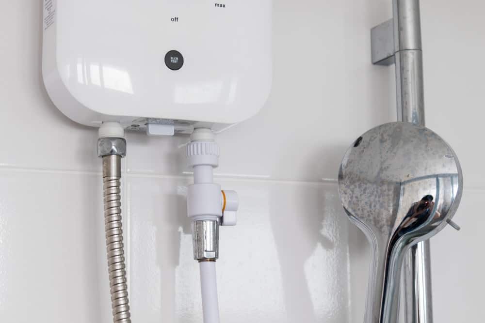 Un cuarto de baño con azulejos blancos y un calentador eléctrico blanco junto a la ducha telefónica.