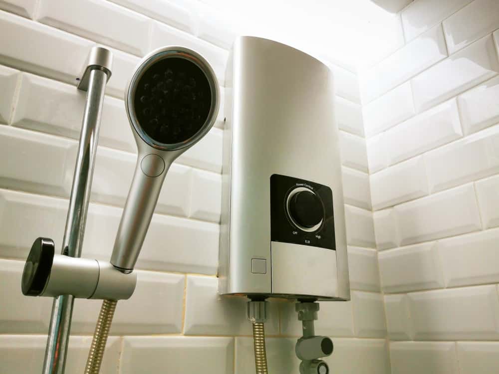 Esta es una vista de cerca del cabezal de la ducha de un baño con un calentador eléctrico al lado.