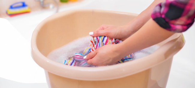 Mujer lavando la ropa a mano en un lavabo de plástico beige