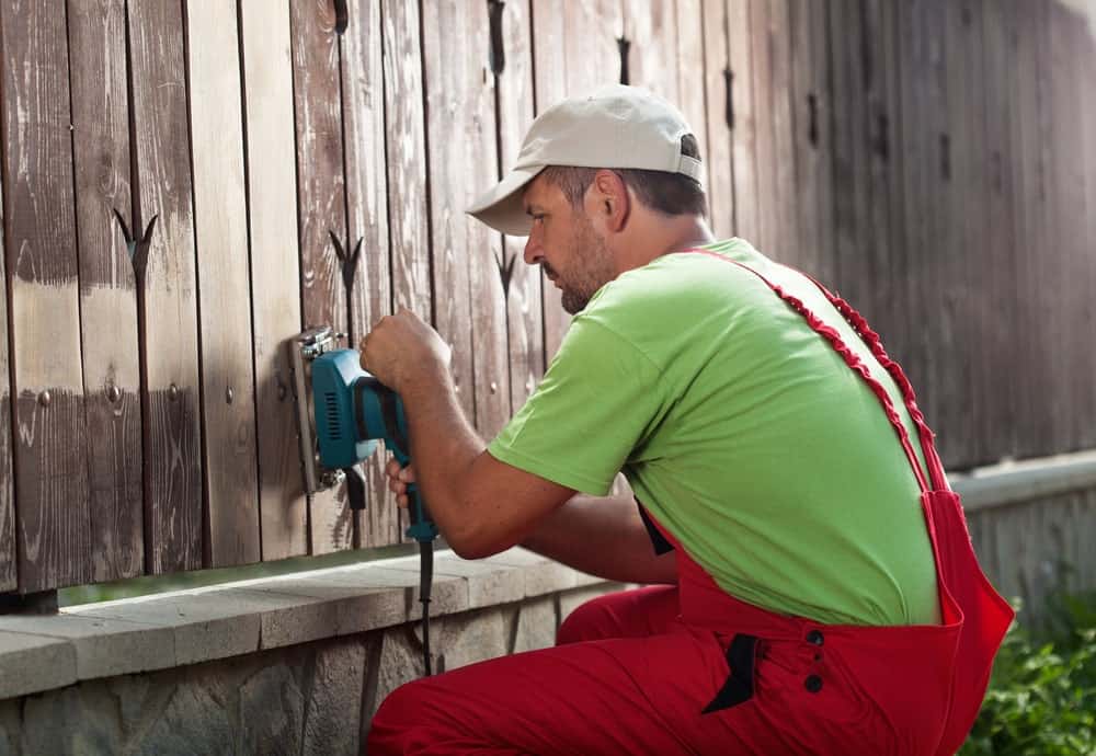 Hombre utilizando un decapador eléctrico en las paredes de madera de su patio trasero.