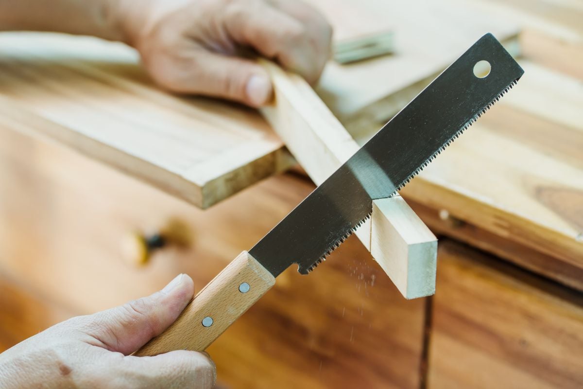Un hombre utiliza una sierra japonesa para cortar un pequeño trozo de madera.