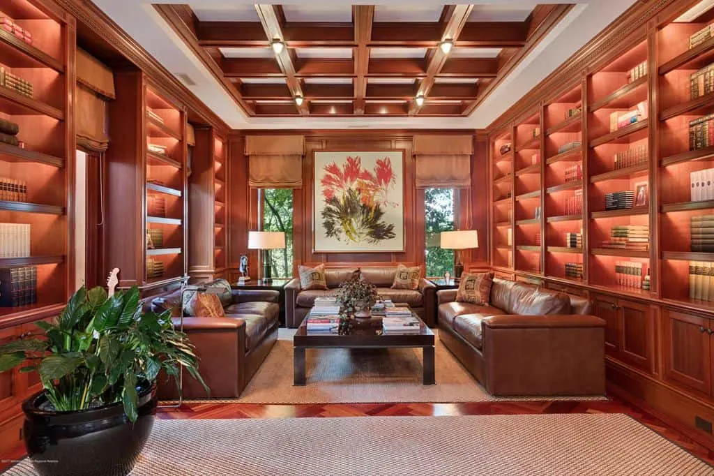 Una lujosa biblioteca doméstica con elegantes sofás y múltiples estanterías junto con un elegante techo artesonado.