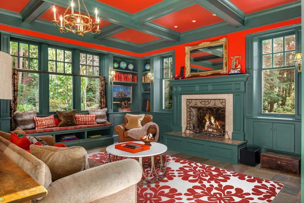 El diseño del techo artesonado encaja en un acogedor estudio con paredes verdes y detalles rojos. Hay una gran chimenea y un banco para sentarse.