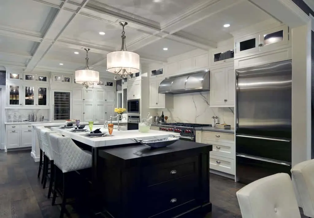 Cocina de transición con techo artesonado, lámparas de araña y electrodomésticos de acero inoxidable.
