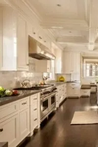 La enorme cocina blanca tiene suelo de madera oscura, armarios de estilo shaker y un artesonado ornamentado.