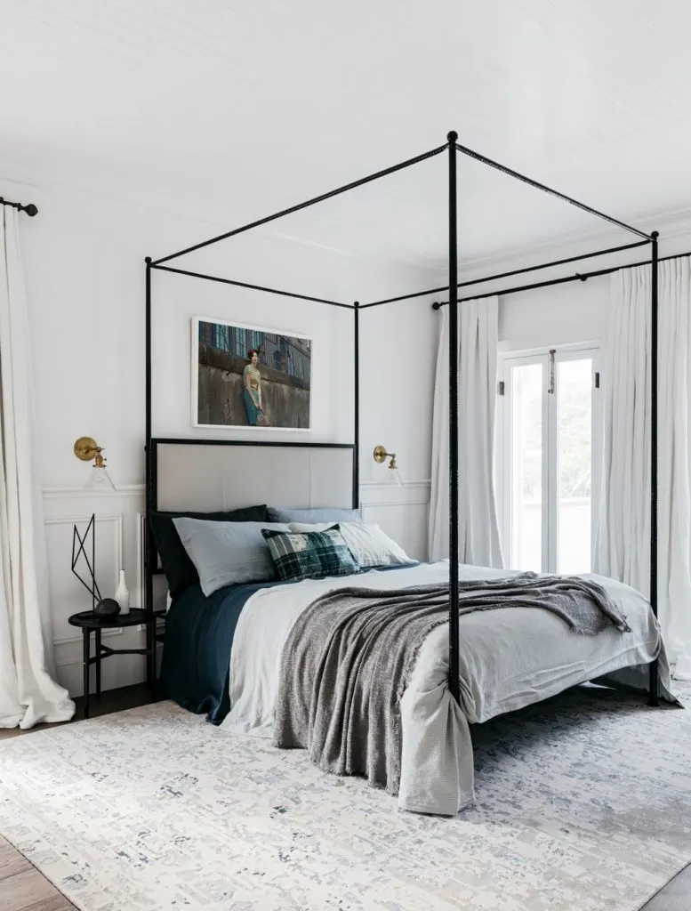 Un plano enfocado de la elegante cama de este dormitorio principal colocada sobre la alfombra que cubre el suelo de madera de la habitación.