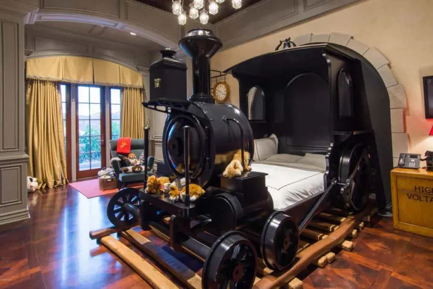 Una mirada centrada en la cama diseñada a medida con forma de tren de este dormitorio infantil. La habitación tiene un techo alto, paredes grises y un elegante suelo de madera.