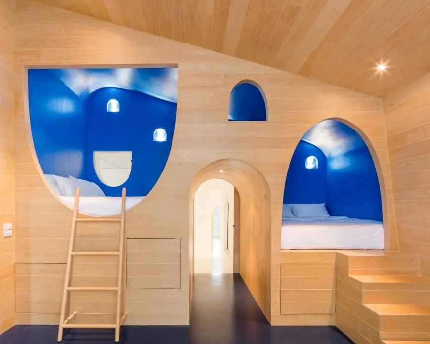 Una mirada centrada en el juego de cama hecho a medida de este dormitorio infantil con una escalera y una escalerilla, junto con paredes azules. La habitación también tiene un techo de cobertizo de madera.
