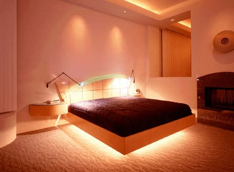Un vistazo más de cerca a la impresionante cama a medida de este dormitorio principal, iluminada con luz brillante, junto con mesillas de noche empotradas. La habitación tiene techo de bandeja y suelo de moqueta.