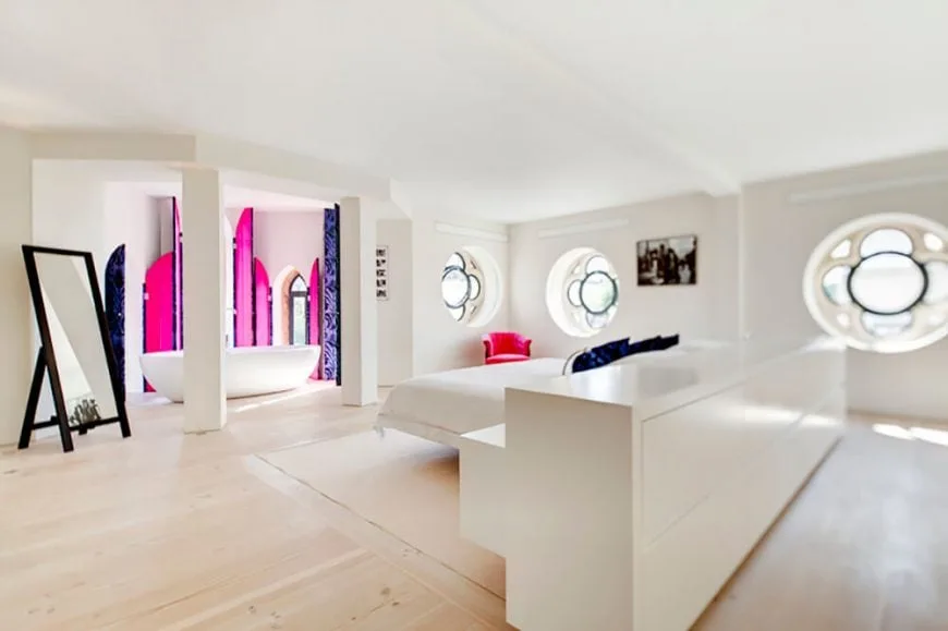 Gran suite principal personalizada que presenta una moderna configuración de cama con mesillas de noche empotradas junto con una bañera independiente en el lateral. La habitación tiene suelo de madera, paredes blancas y techo blanco.