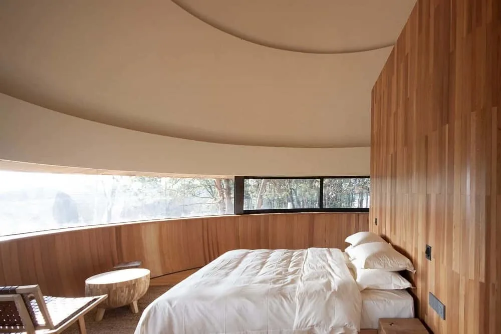 Ésta es una vista del dormitorio con un estrecho conjunto de ventanas de cristal que recorren el centro de la pared curva frente a la cama empotrada en la pared de madera del cabecero.