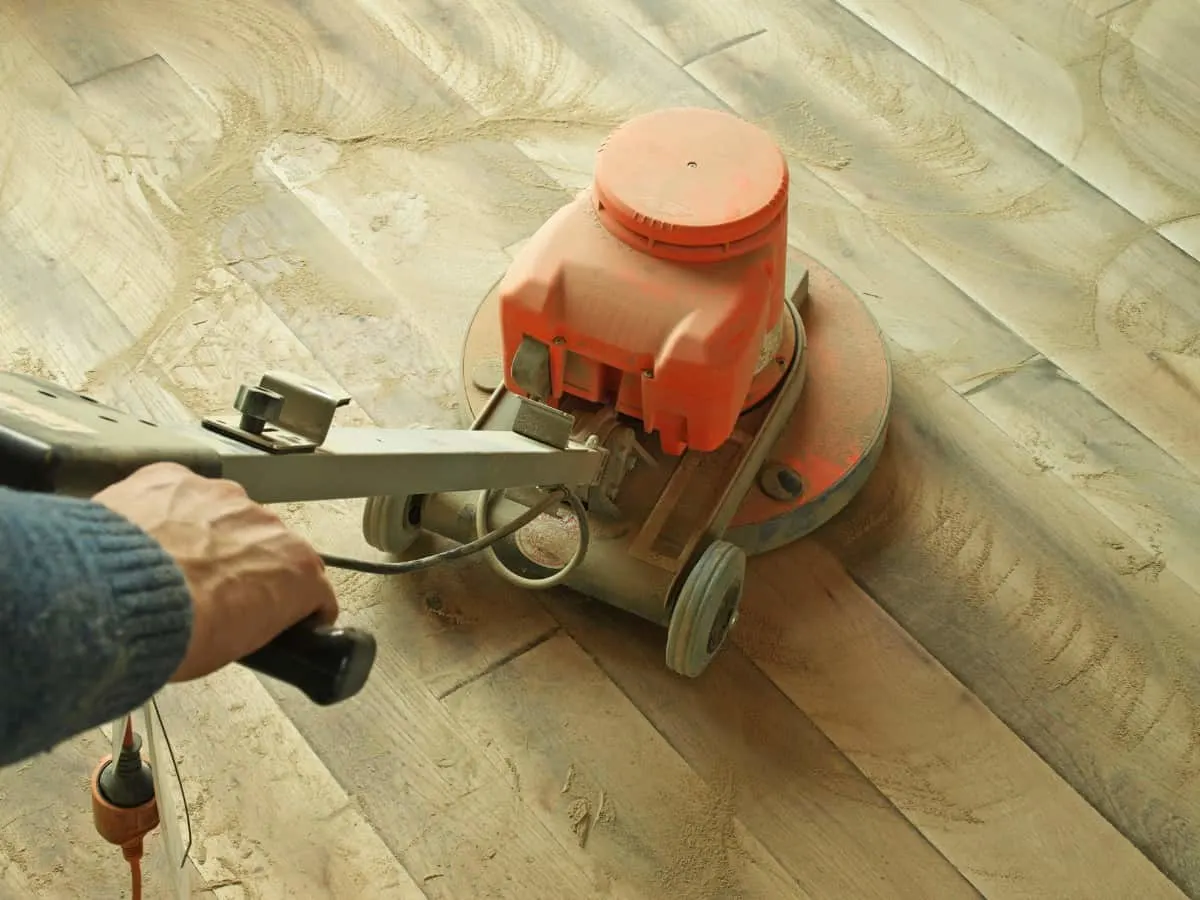 Hombre puliendo un suelo de madera utilizando una lijadora para suelos.