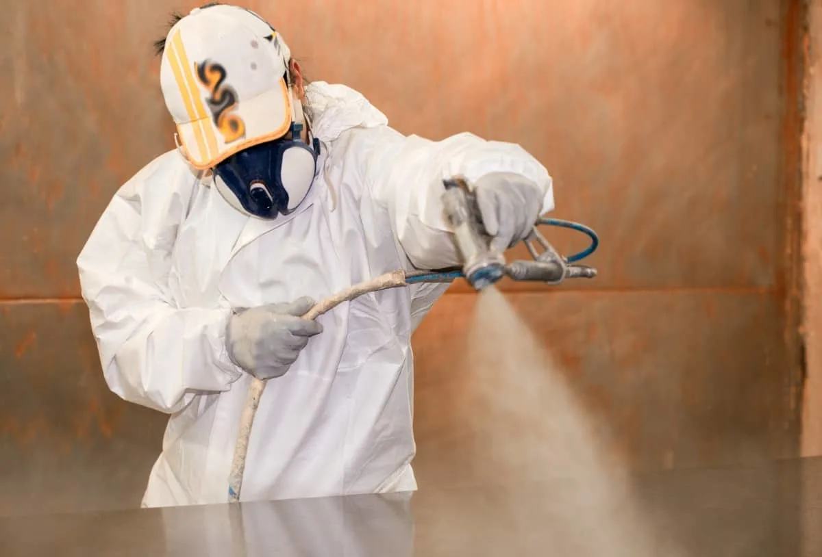 Mujer con traje de seguridad pintando una tabla con spray.