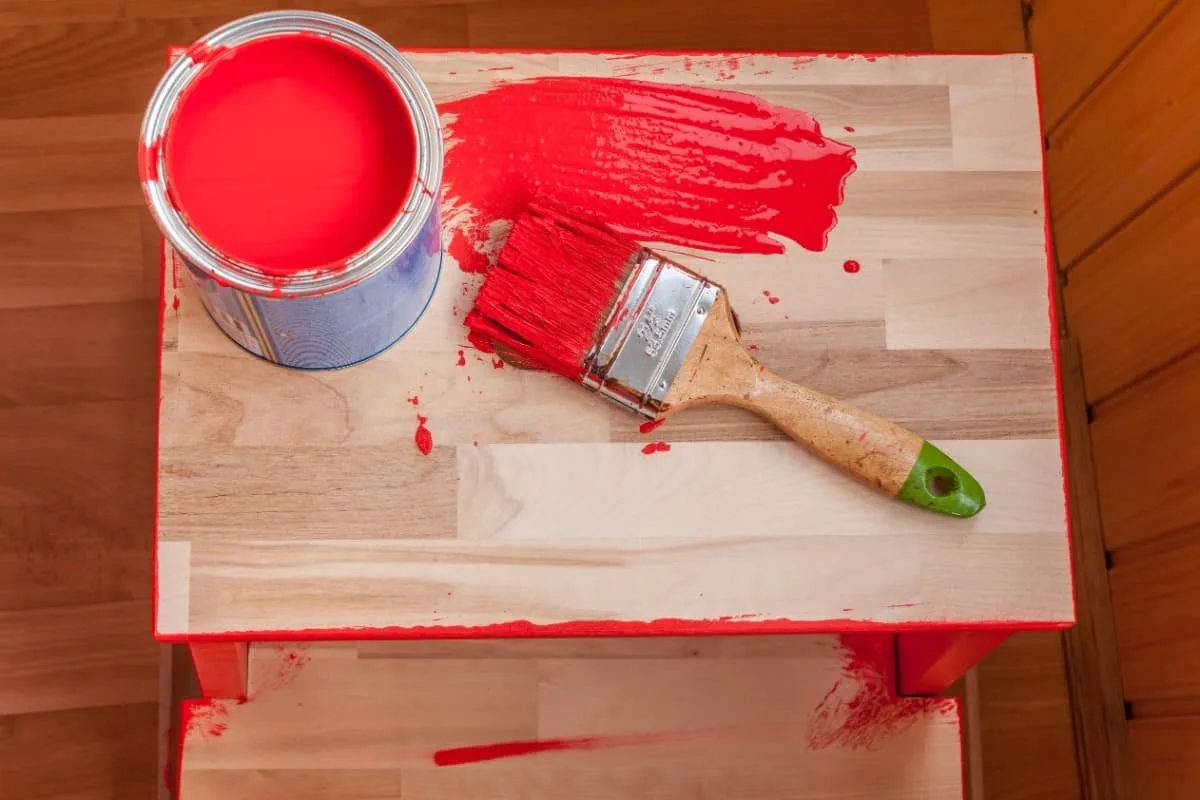Pintura roja y pincel sobre silla de madera.