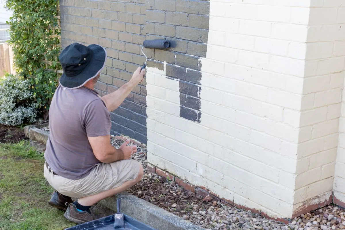 Un hombre pintando una pared de ladrillos con blanco.