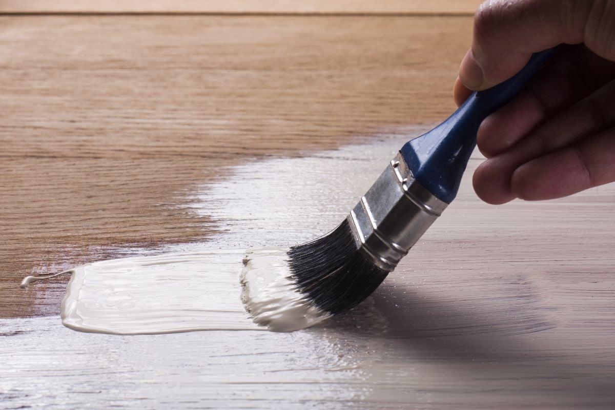 Una persona aplicando pintura de esmalte sobre una madera.