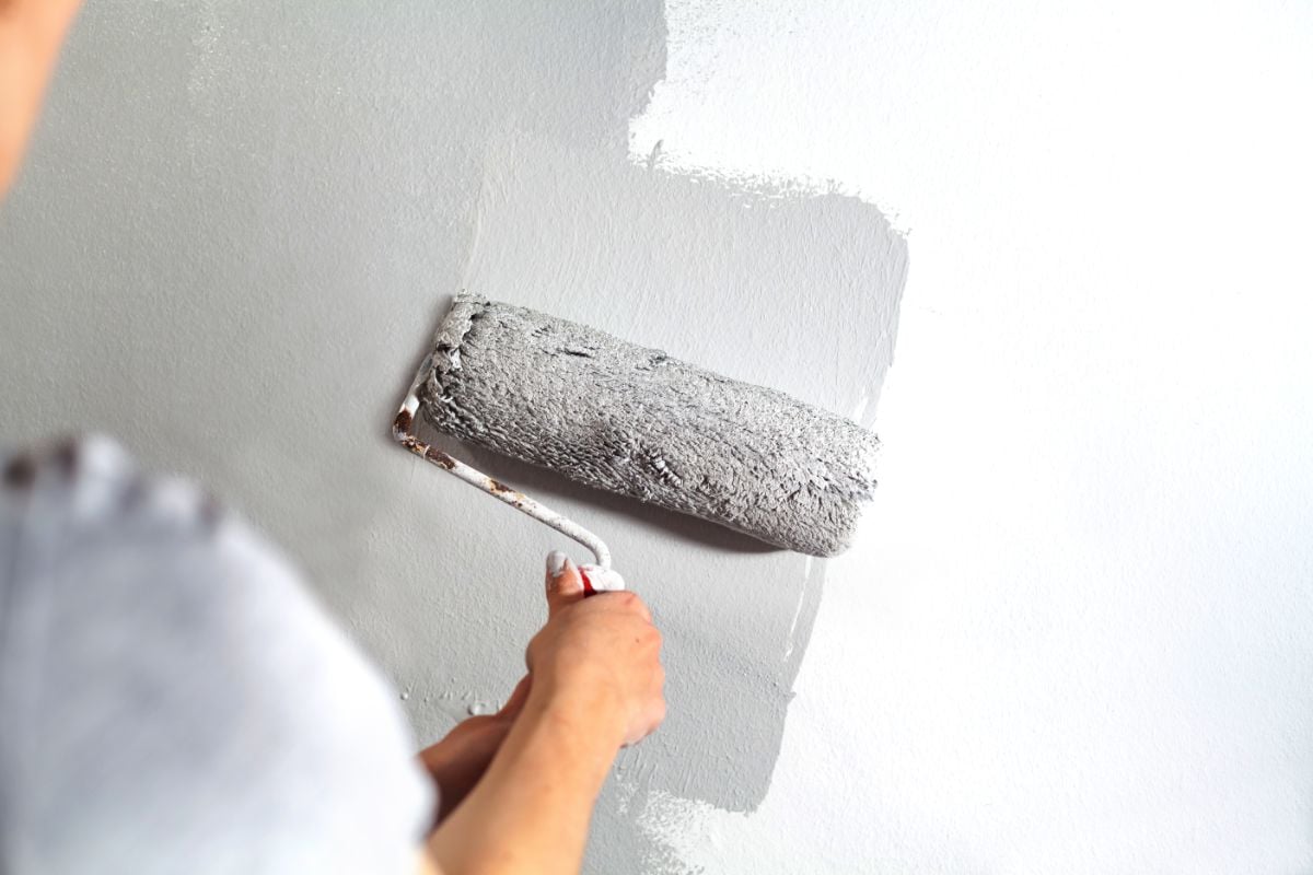 Persona aplicando pintura gris con brocha de rodillo.