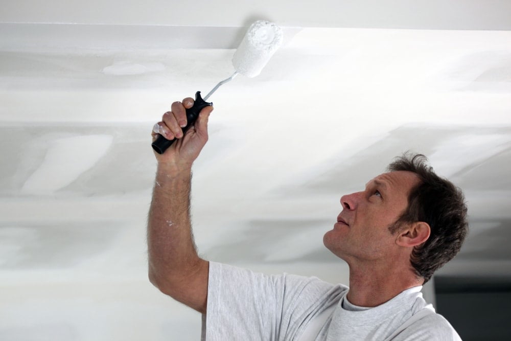 Un hombre está pintando el techo con pintura blanca satinada.