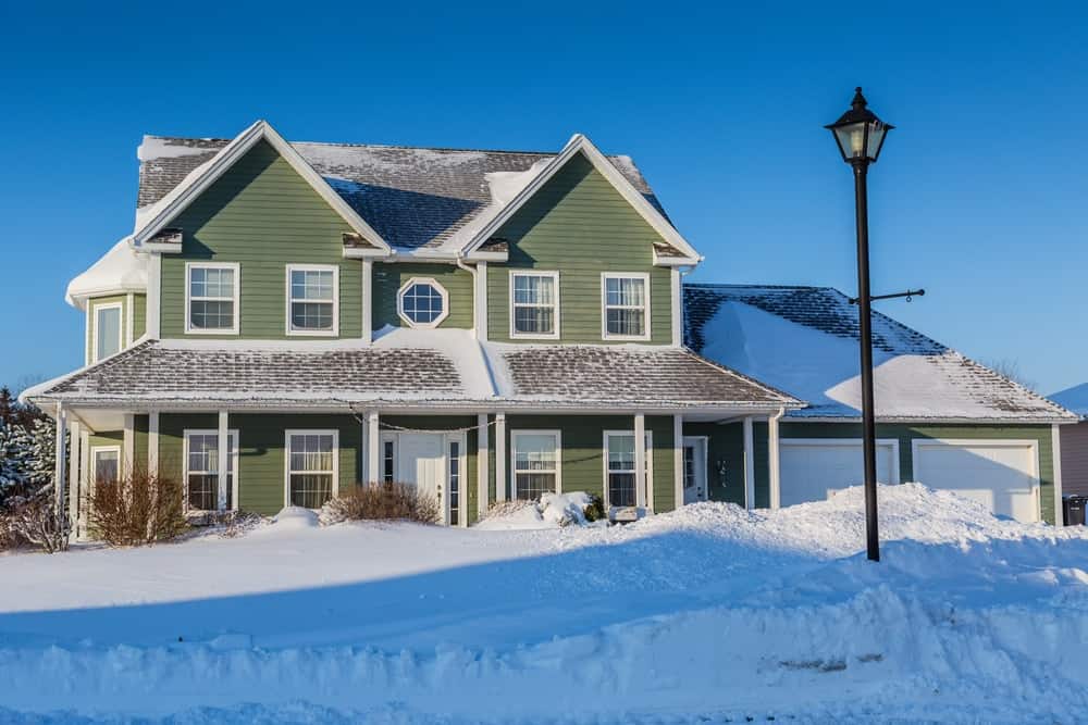 Casa unifamiliar norteamericana con revestimiento exterior verde después de una tormenta de nieve.