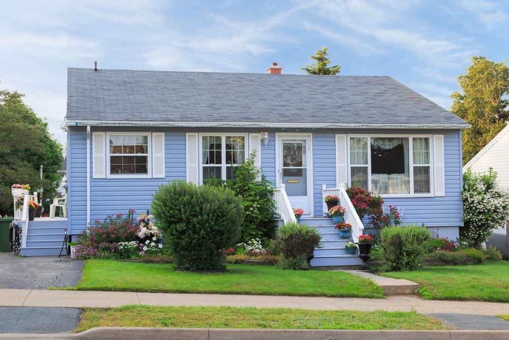 Vista de la calle de una casa bungalow de los años 60 con revestimiento exterior azul.